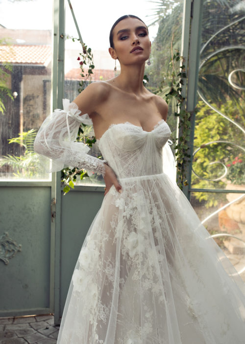 Woman in greenhouse. hands on hips to showcase her detachable voluminous sleeves that compliment her soft corset a line bridal gown