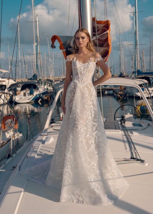 Bride on boat at a bay. Sun rises with the bride standing in front of stand. Off shoulder a-line gown adorned with sequence, beading, and manually sewn detailing.